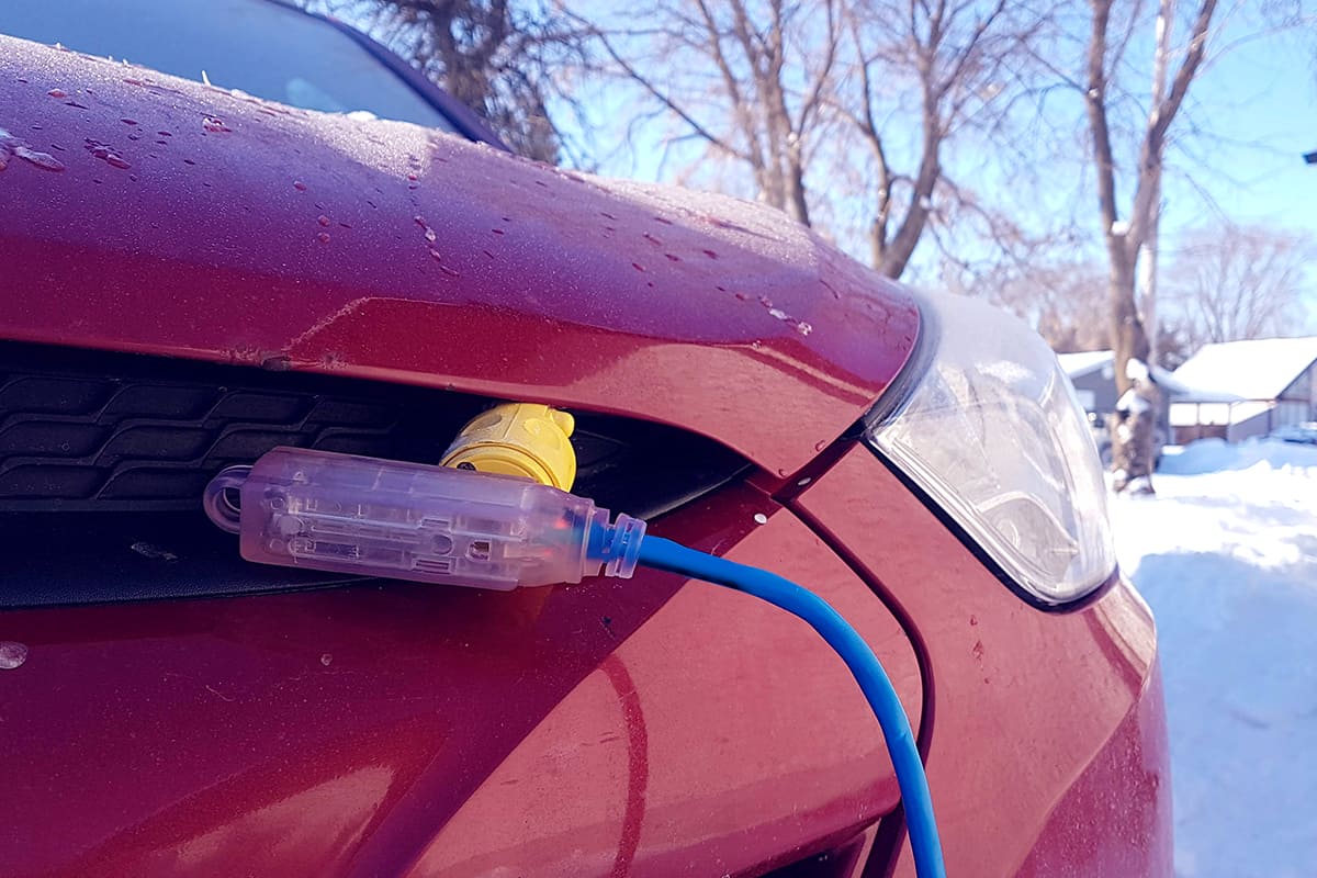 Block heater cable plugged into a vehicle parked in a snowy winter driveway