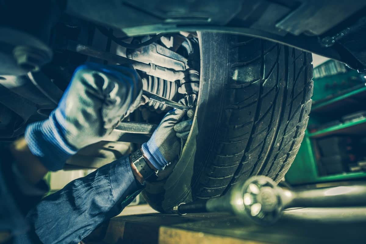 Car Mechanic Fixing Tie Rod and Steering System While Being Under the Vehicle. 