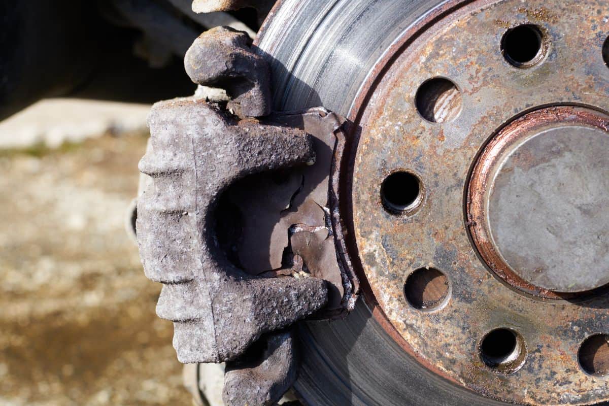 Close up view of a damaged car brake pad and rusty spoiled rotor under sun shine