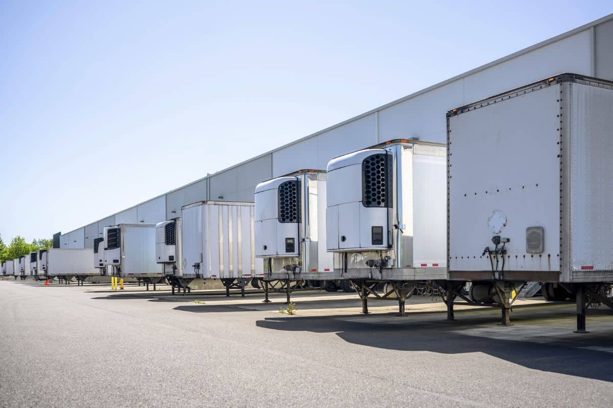 Industrial grade refrigerator and dry van semi trailers with reefer units on the front wall and without it standing at warehouse dock gates loading commercial cargo for next freight delivery.
