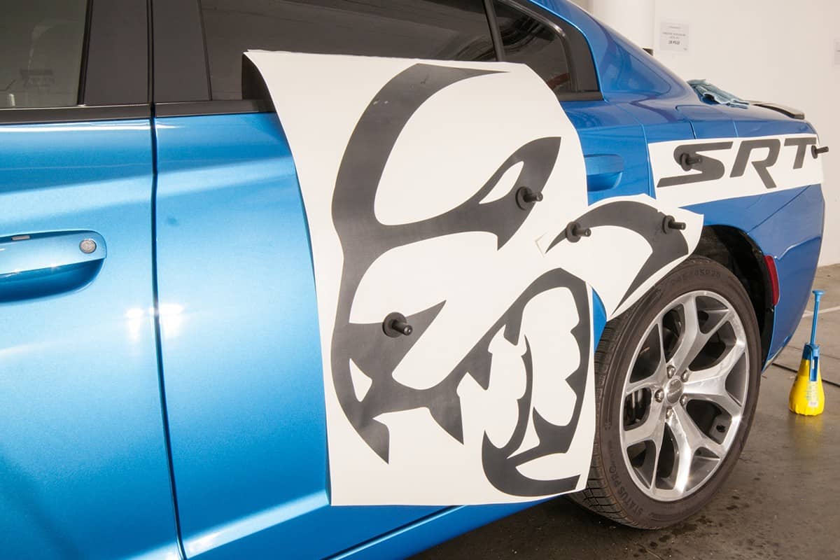 Installation of black foil decals on a blue luxury fast car in the garage