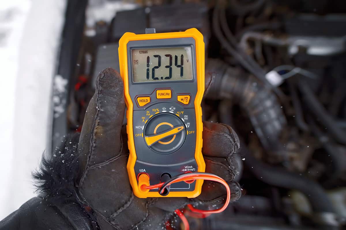 Mechanic test car electric system with multimeter, check car battery voltage.
