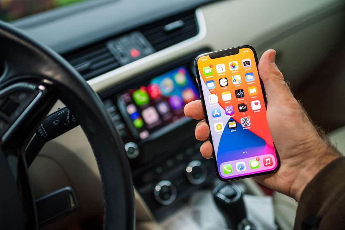 male driver holding new iPhone 12 Pro smartphone with infotainment car computer