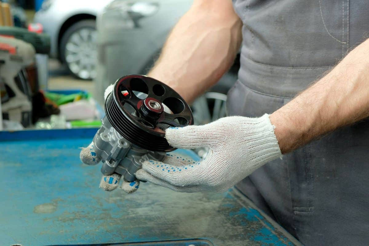 The power steering pump is in the hands of an auto mechanic. Close-up. Inspection of the new spare part before replacement during repair and maintenance of the car.