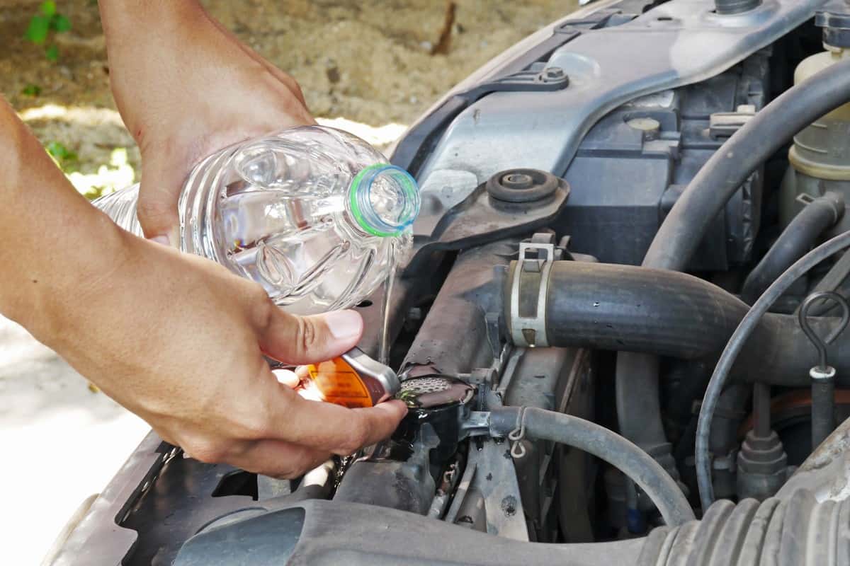 man doing car regular maintenance. hand pouring water into radiator tank from a clear bottle
