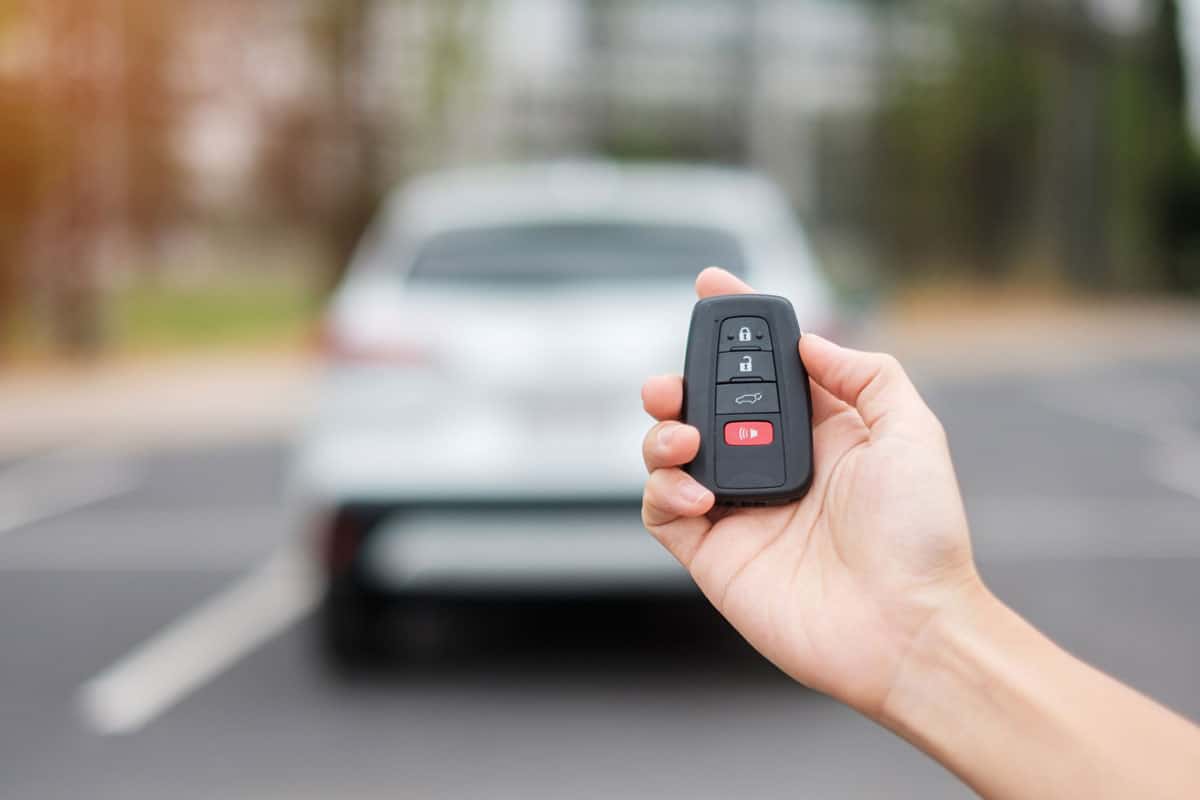 Hand holding car remote control, smart key to lock or unlock doors of white car. Safety, travel and transportation concept 