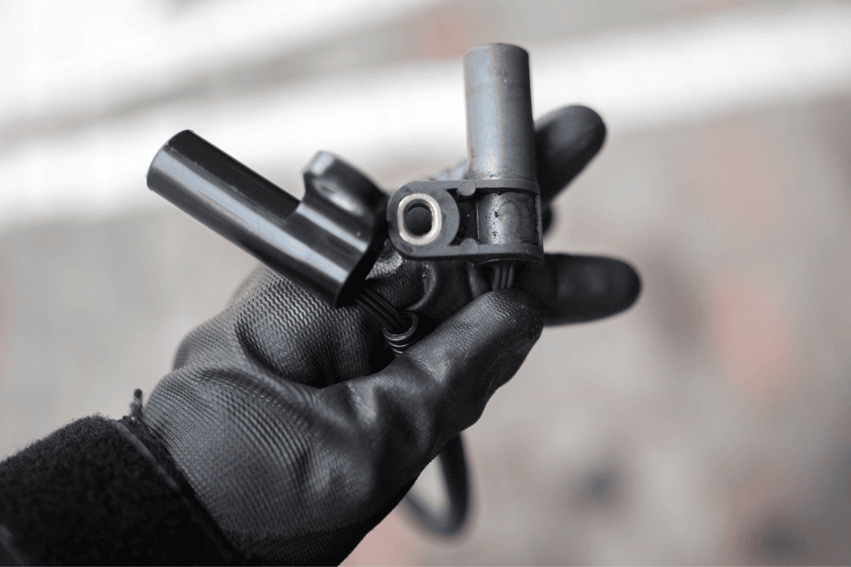 Electromagnetic crankshaft position sensor of a car engine in the hands of an auto mechanic