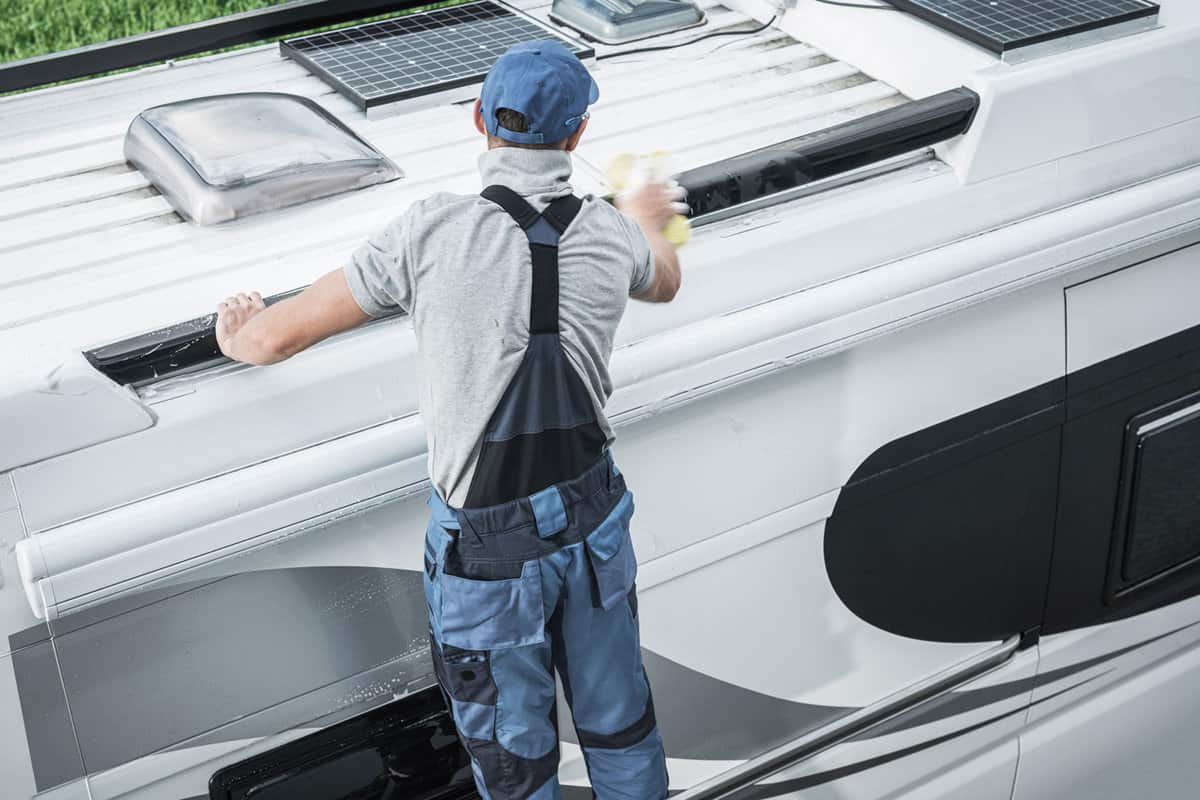 Recreational Vehicles Industry Theme. Caucasian RV Service Worker Washing Camper Van Roof Using Large Soft Sponge and Cleaning Detergent.
