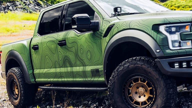 2021 Ford Raptor Roush with a green wrap driving over rocks with fender flares1600x900
